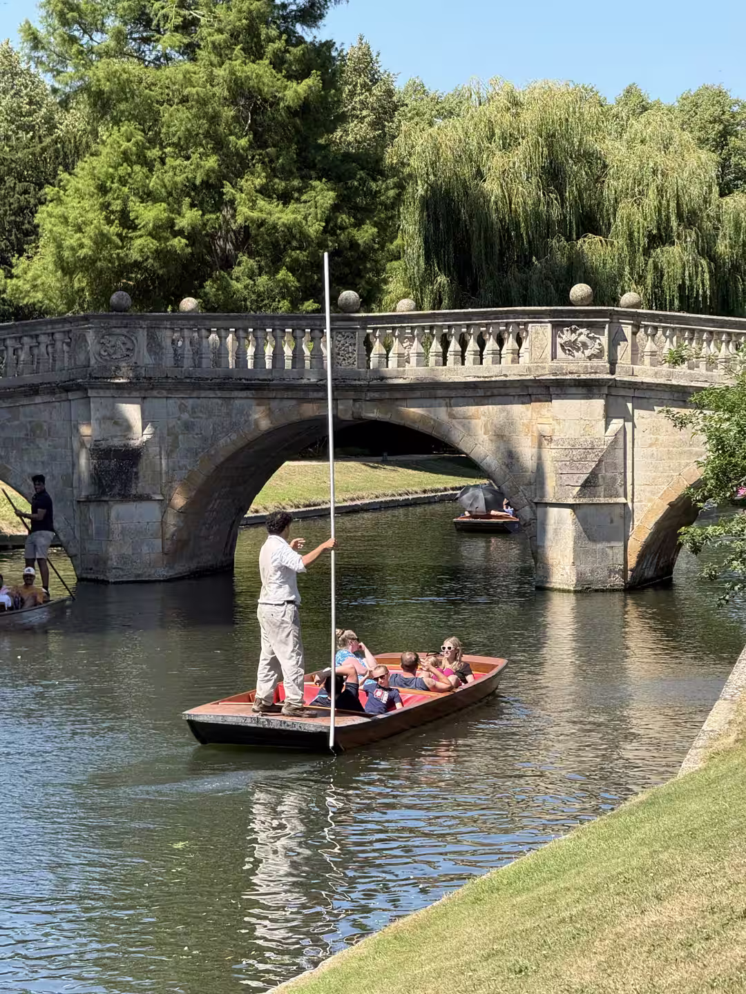 A punt being poled under a stone bridge on the Cambridge College Backs