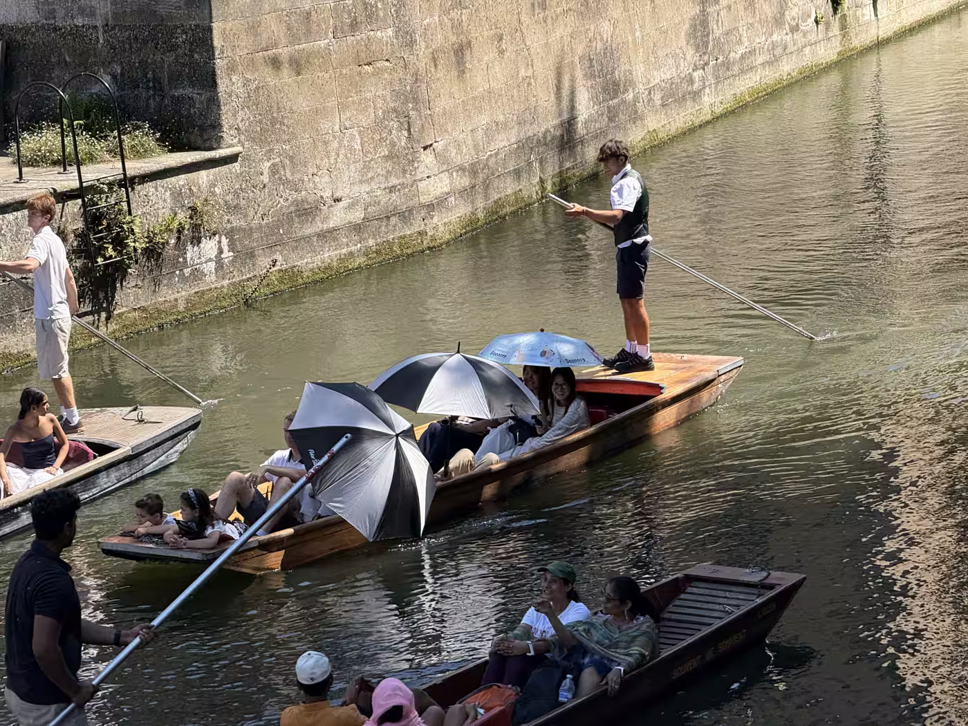 Passengers under parasols on a shared punt on the River Cam, Cambridge
