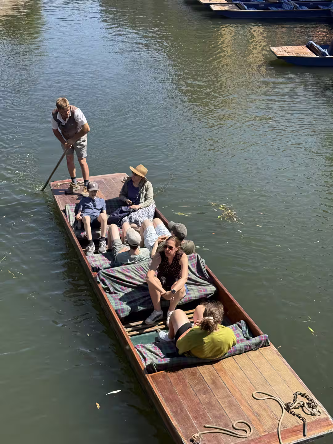 Passengers relaxed in a shared punt on the River Cam, dressed for a summer day in Cambridge